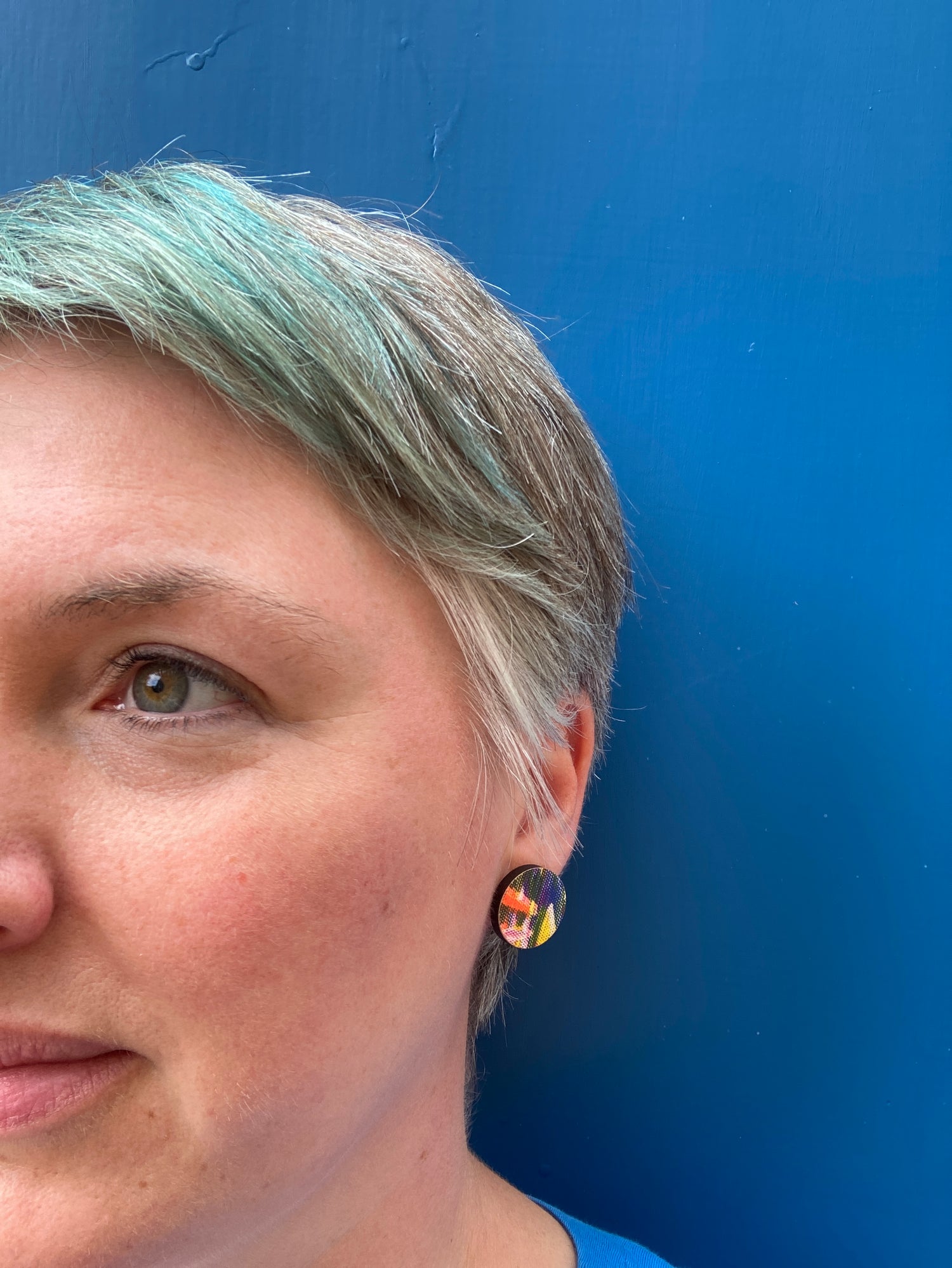 A photograph of me, a woman against a blue background. Half of my face is in the photo, showing off my large stud riso earrings!